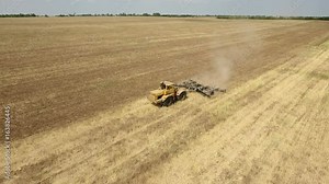 Astonishing view on a farm tractor drawing a spike harrow to remove wheat straw and to do a tillage from a bird`s eye perspective in Eastern Europe in a sunny day. The rural landscape is fine