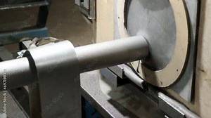 Industrial manufacturing machine pressing the tube against the rough surface for grinding. Factory machine manufacturing the steel tubes. Tube manufacturing machine operating at the facility.