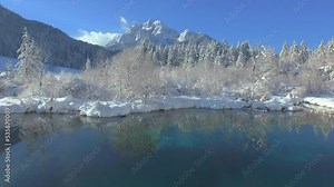 AERIAL: Flying from water reflection at Zelenci towards snowy Ponce Mountains. Magnificent view of snow covered mountain landscape and crystal spring water at Zelenci. Stunning winter moment in alps.