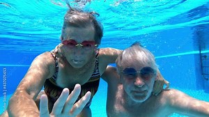 Senior old couple have fun together underwater in blue water pool enjoying summer holiday vacation and healthy lifestyle - happy mature people under water happy lifestyle - aged man and woman