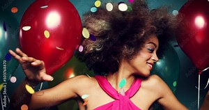 Carefree young woman at a party dancing between colourful balloons and confetti feeling joy. Young woman having fun dancing and shaking her afro at a party. Happy woman dancing between balloons