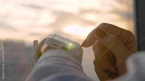 Close up: woman hand using wearable white smartwatch device against warm sunset sky - scrolling and touching - slow motion. Sun lens flare, golden hour. Relax, leisure time and technology concept