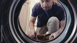 Close-up of young adult bearded man who puts his clothes inside the washing machine. View from inside the washing machine. Laundry day concept