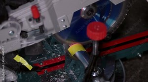 Cutting an aluminum part with a chop saw. Side view of the fast spinning blade used for machining round metal material. Industrial work in a dark outdoor environment. Dust and chips flying around.