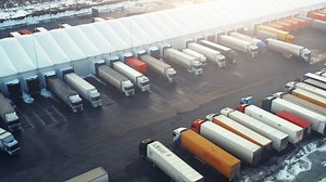 Semi-trailers trucks stand at warehouse ramps and on a parking lot for load and unload goods in a big logistics park. Aerial view