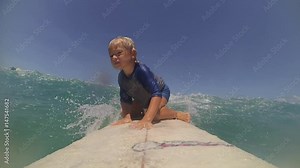 Child learning surfing with young father in tropicals. Cute boy on surfboard on ocean wave. Enjoying summer vacation in surf camp. POV