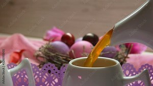 Easter table setting for the festive breakfast: a tea poured in the cup on the background of colored pink Easter eggs in the nest