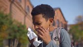 Close-up portrait of teen African-American boy sneezing and blowing...