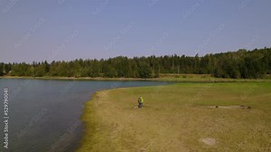 Drone video of woman wearing a green rain jacket walking near the water's edge of Alder Lake, Washington.