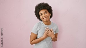Grateful african american woman beaming, hands resting on chest in heartfelt gesture, donning t shirt and isolated on a popping pink backdrop. proud, healthy confidence personified.
