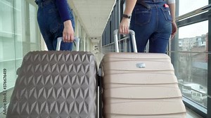 Two travelling girls walking away with luggages while waiting for transport. Young girl pulling suitcase in modern airport terminal