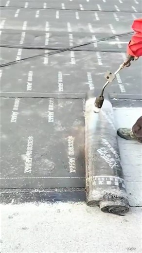 installing a black waterproof roll manually using a hot flame in a professional construction area