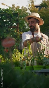 Male gardener with hose watering vegetable garden while his female colleague taking care of the plants