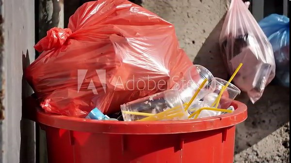 Red trash can overflowing with plastic waste and red bag