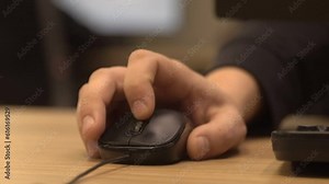 Office worker scrolls black computer mouse wheel with index finger on wooden table on blurred background extreme closeup