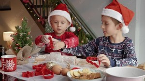 Happy smiling boys in Santa's hats making cookies and cutting dough while preparing for Christmas. Winter holidays, celebrations and party