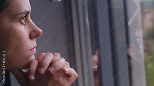 Сlose up stressed young woman looking outside through window, thinking of personal, reflecting alone. Frustrated girl feeling lonely at home, suffering from depression, thinking, solitude concept