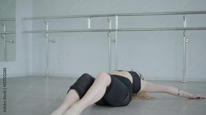 Fit girl in black clothes performing contemporary. Female dancer shows flowing motions, body and hands waves at white room. Modern ballet dance choreography. Young woman is moving smoothly