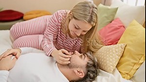Affectionate woman embracing loving man, lying together in a colorful, cozy bedroom setting.