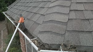 Cleaning out dirty, blocked gutters from the ground, with a plastic scoop on a pole.