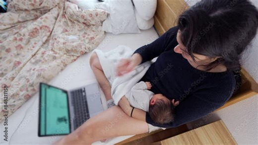 Mother multitasking with laptop while holding a newborn baby, balancing remote work and parenting, highlighting the challenges and dedication of modern working mothers