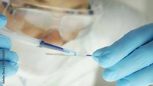 detail of a researcher with azure gloves pouring drops on a slide