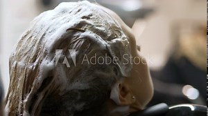 Blonde woman gets her hair washed with shampoo by hairdresser. Slow-motion close-up