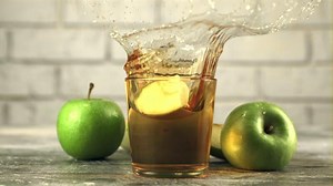 Super slow motion in a glass with apple juice drops a piece of apple with splashes. On a white background. Filmed on a high-speed camera at 1000 fps.