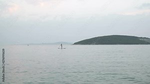 Girl stand up paddle boarding (sup) on quiet sea at sunset. long shot