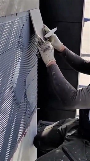 Carefully spreading adhesive on a wall and installing large grey tiles for a modern outdoor finish