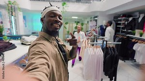 Man filming POV vlog while doing shopping in elegant fashion boutique, assisted by friendly shopkeeper. Influencer doing social media content in clothing store, receiving info from woman