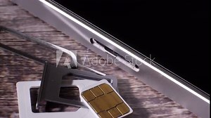 Closeup shot of the sim card slot of a silver colored smartphone. Showing the tool needed to open it. Modern technology. Wood background. Communication. Camera slowly moving around.