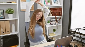 Sleepy young blonde business woman stretching her aching back, yawning away early morning tiredness, seeking relaxation in the office