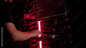 Close up of a man punching the keypad on a computer in a server room with flashing red lights