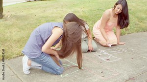 A mother and her two girls sit on the ground and draw a hopscotch court