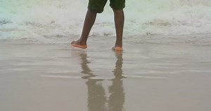 Low section of African american man standing on the beach. Sea waves splashing on his legs