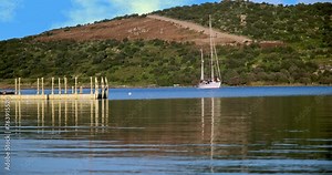 This breathtaking landscape video offers the magic of serenity and nature. The sailboat gently swaying on the pier, the deep blue sea and the green mountains in the distance come together to create