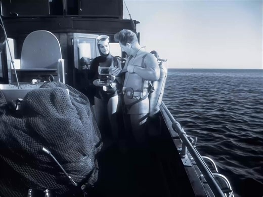 Gear up for glory in “The Guinea Pig” snippet #3—our virile frogman Mike Nelson and his curvaceous ex Jennie Wallace (Jan Brooks, squeezing those luscious assets into a skin-tight wetsuit that hugs every tempting curve) strap on their SCUBA seduction aboard the dive boat she chartered. Watch as they buckle up those bulging Aqua-Lungs, hoses dangling like forbidden temptations, regulators ready to deliver that greedy gulp of life-sustaining air. Mike’s ripped torso glistens under the straps, whil