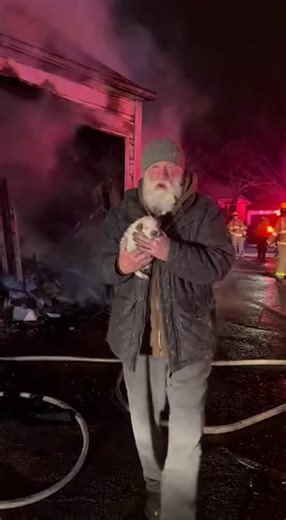 “He walked back into the burning garage — and came out holding something no one expected.” The fire wasn’t even fully out yet. Smoke drifted low across the street. Ash clung to coats. Emergency lights flickered against blackened walls. Neighbors stood frozen, unsure where to look. And then the old man disappeared back inside. White. Late 70s. Thin frame. Gray beard singed unevenly. His jacket smelled of smoke, old fabric, and faint alcohol. His hands shook — not from fear, but from urgency. Fire