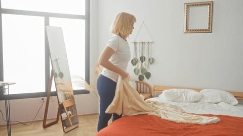 clip-4099285459-woman-smoothing-bed-sheet-hand-while-arranging