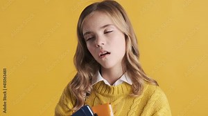Bored blond teenage student girl yawning tired on study want to go home sleep isolated on yellow background. Study concept