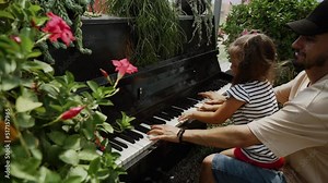 Father teaches daughter to play the piano in the fruit greenhouse