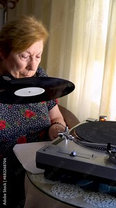 An older woman put a vinyl record on the turntable. Real time video. Stock Video