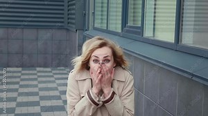 30s surprised woman shocked by the news, emotionally covers her face with her hands, standing in the business district. Young business female with emotional amazed glance staring at camera