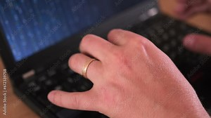 Matrix code on laptop screen, close-up male hands, with wedding ring on finger, typing program code on laptop. Freelancer and work at home concept.