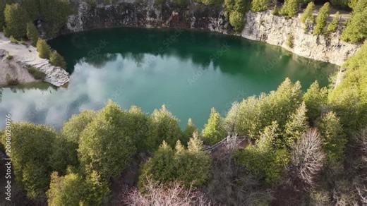 A wide aerial shot of the historic Elora Quarry Conservation Area in Ontario, showcasing its two-acre emerald swimming hole encircled by dramatic 12-meter limestone cliffs and dense forest