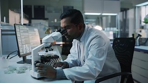 Un chercheur en recherche médicale effectue des expériences ADN au microscope et rédige des résultats sur ordinateur de bureau dans un laboratoire de sciences biologiques. Laboratoire multiethnique diversifié avec des ingénieurs en blouse blanche.