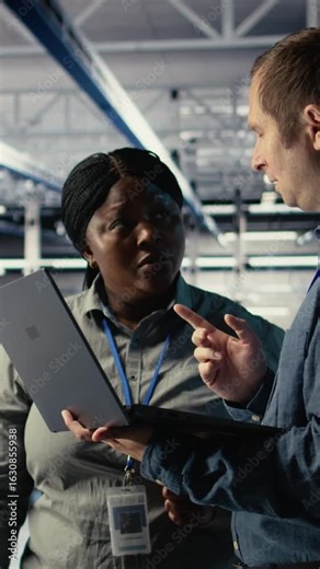 Vertical video Team of data center engineers investigate neural networks configuration, making adjustments. Teamworking server hub coworkers use notebook to check deep learning errors, camera A