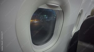 Airplane passenger looking through plane window at airport. Night flight delay