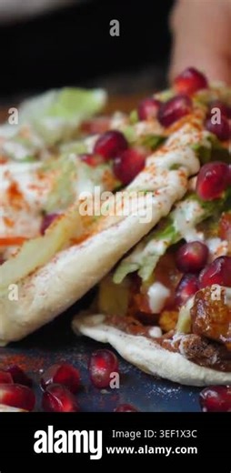 Close up view of a hand taking a delicious middle eastern pita sandwich filled with meat, fresh lettuce, tomatoes, creamy sauce, and topped with vibrant pomegranate seeds and paprika Stock Video Footage - Alamy